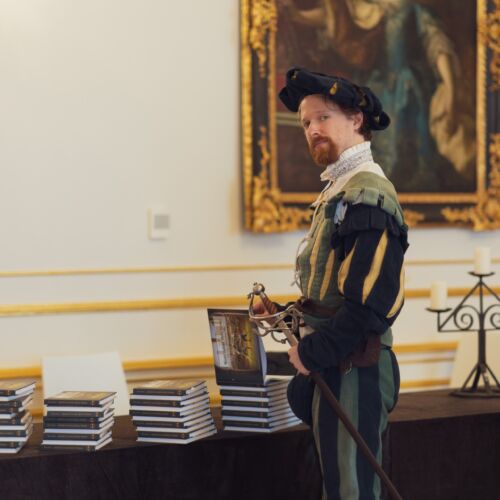 Renesančný šermiar pred stolom s knihami